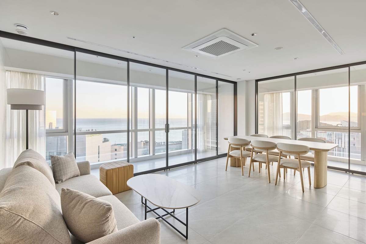 A modern living room with a large sofa, a coffee table, and a dining area with chairs and a table.