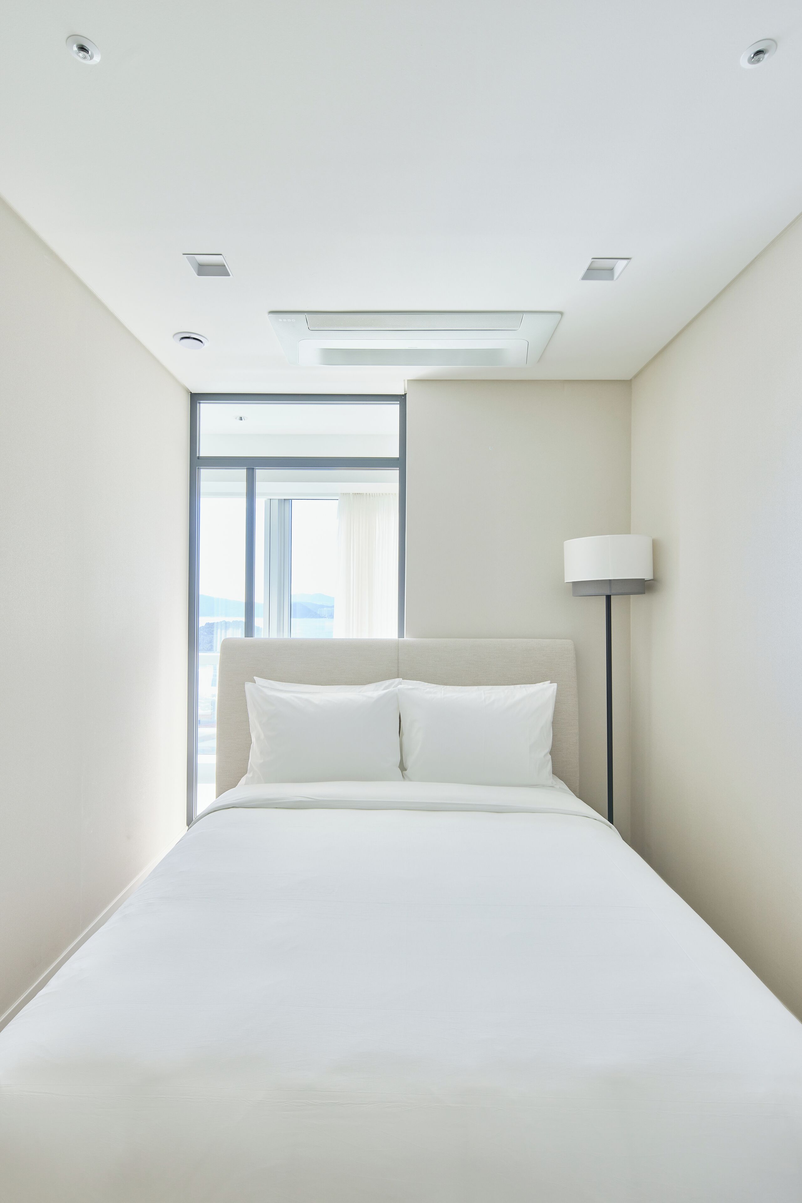 Moderni hotellihuone, jossa on suuri sänky, lattiavalaisin ja suuri ikkuna, josta avautuu näkymä kaupunkiin.