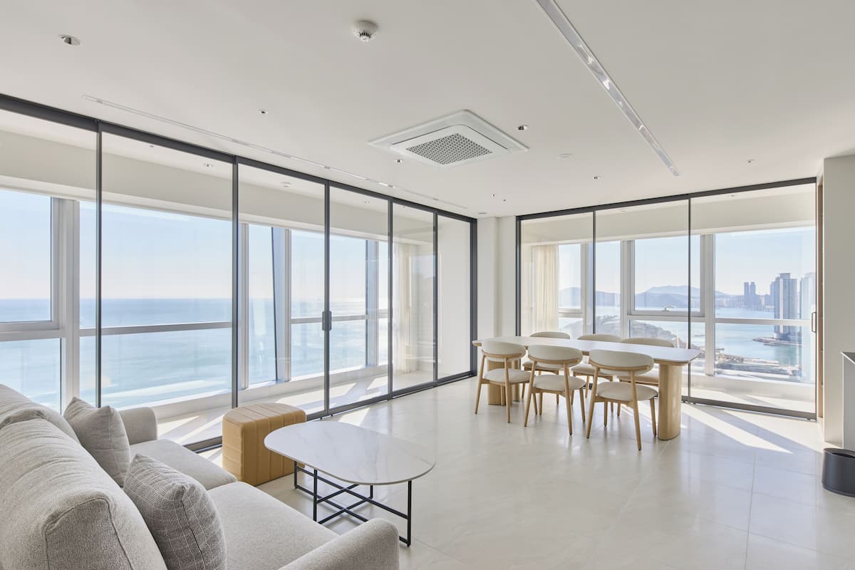 A modern hotel room with large floor-to-ceiling windows, a minimalist interior, and a view of the ocean and city skyline.