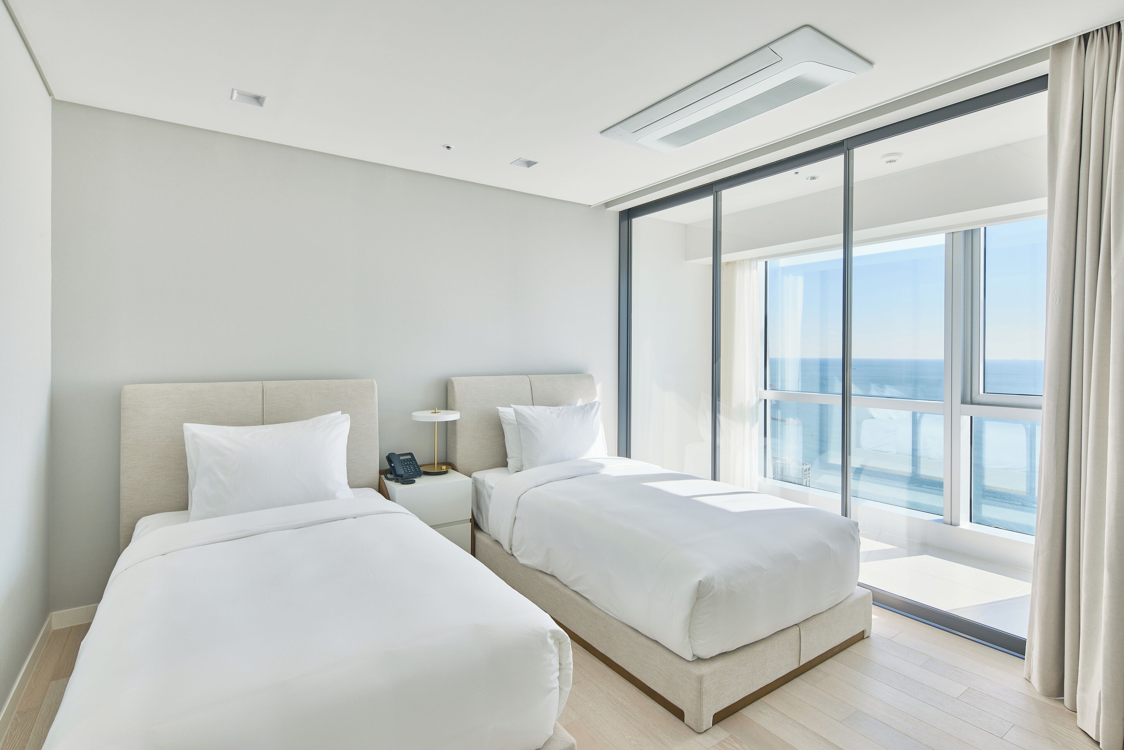A modern hotel room with two beds, a large window with a view, and a sliding glass door.