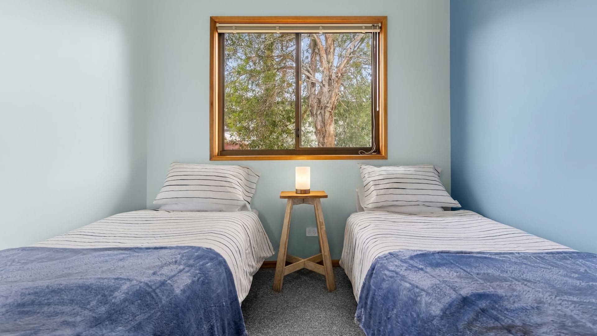 A room with two beds, a window, and a nightstand with a lamp.