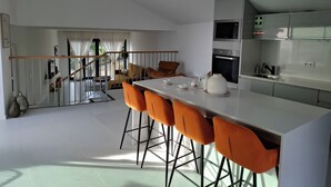 A modern kitchen with a central island, bar stools, and a staircase leading to a balcony. - family and groups escape with  views , sunrise and sunsets in a quiet corner  (Calheta)