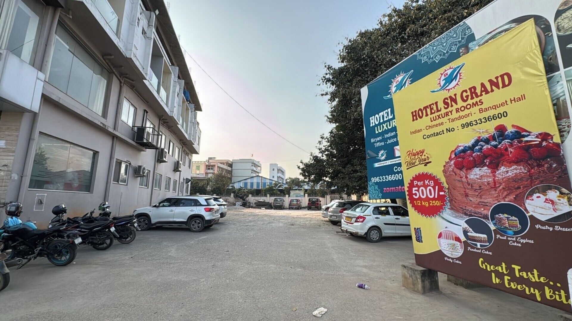 Een hotelschiltje dat Hotel SN Grand adverteert met faciliteiten zoals Indisch, Chinees en Tandoori eten, en telefoonnummer 9963336600.