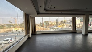 A spacious room with a large window offering a view of a busy street and buildings. - Hotel SN Grand (Maheshwaram)