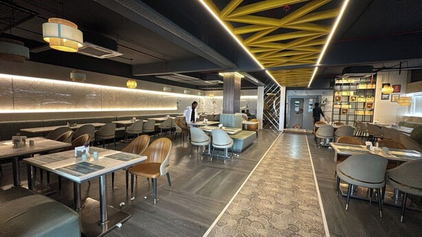 A modern restaurant with a central bar area, seating with high tables, and a patterned carpet. - Hotel SN Grand (Maheshwaram)