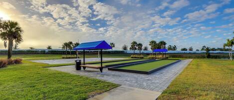 A pool table area with a blue-roofed pavilion, surrounded by well-maintained grass and a clear sky.