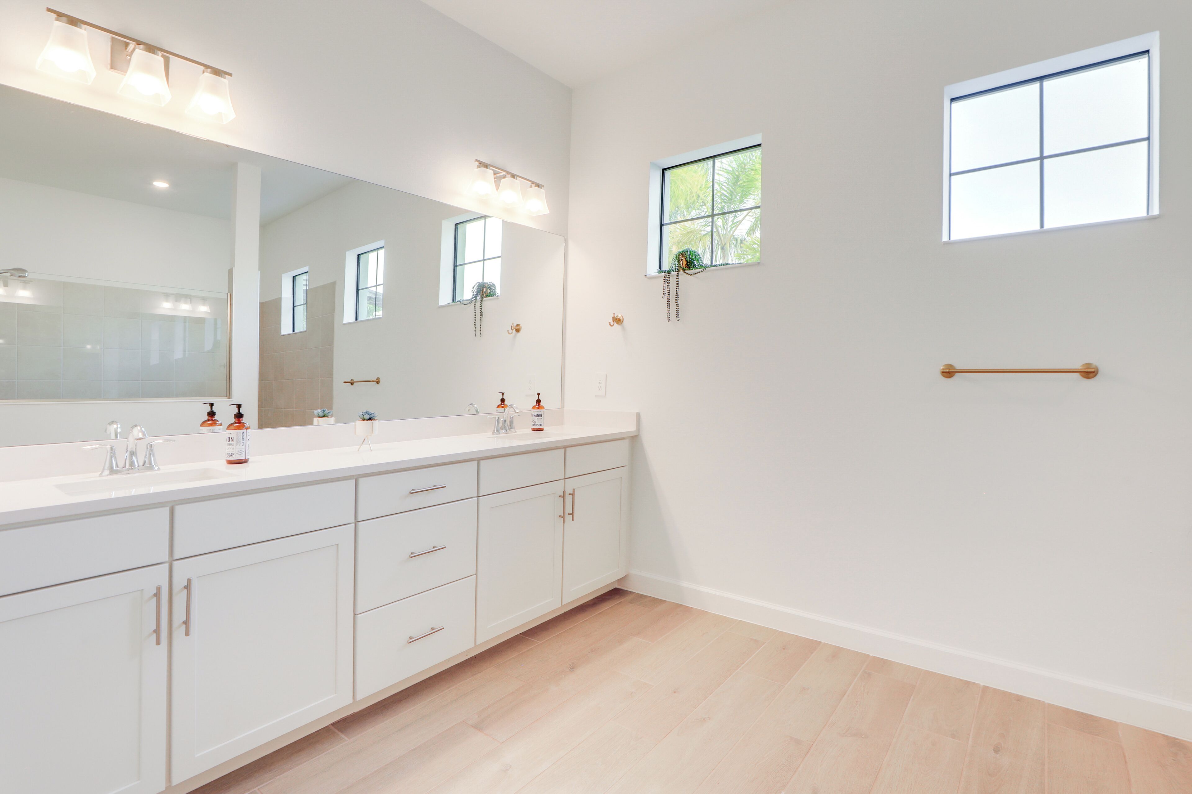 A modern bathroom with a large mirror, two sinks, and a window.