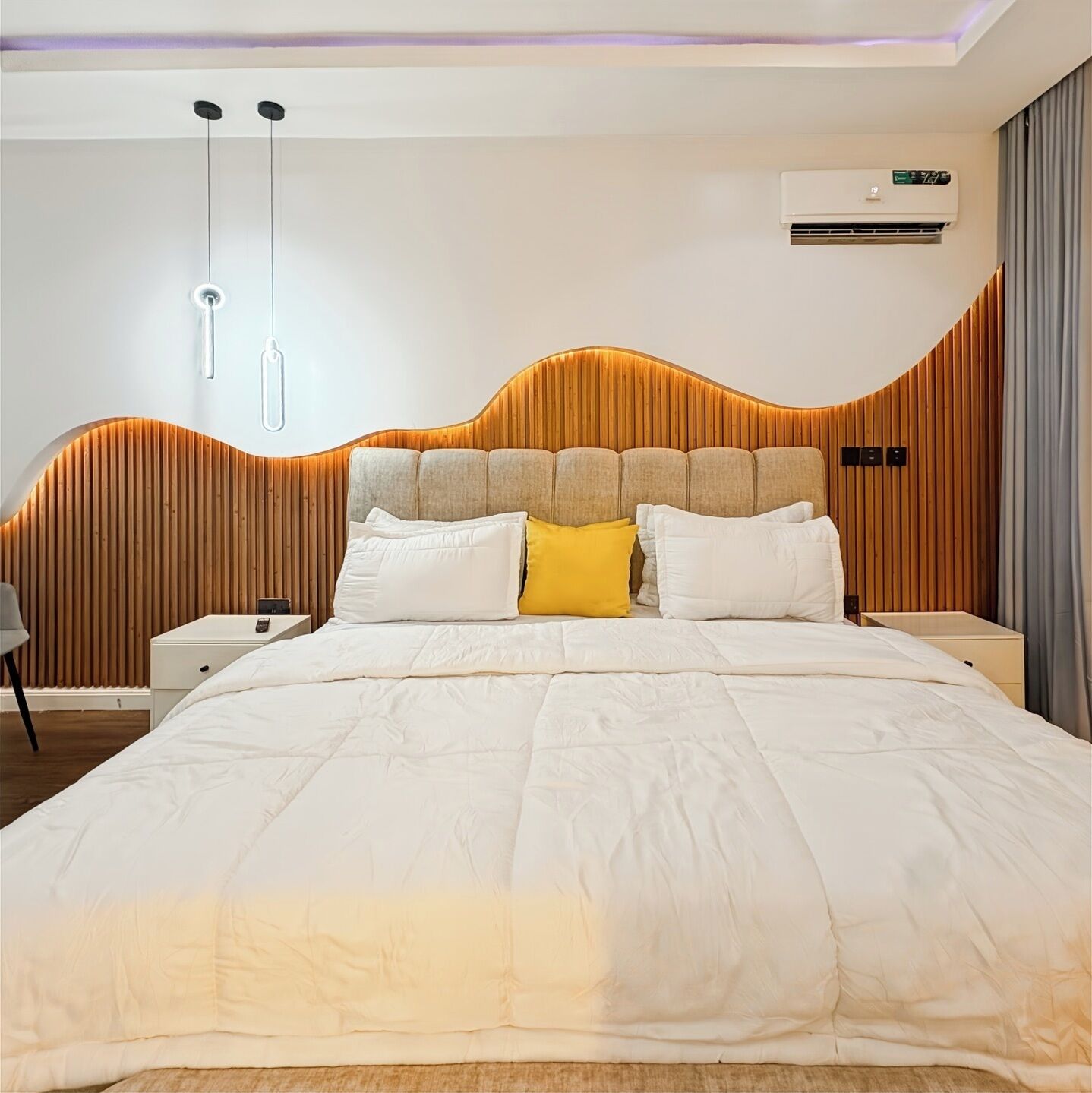 A modern bedroom with a large bed, a wooden headboard, and a wall-mounted air conditioner.