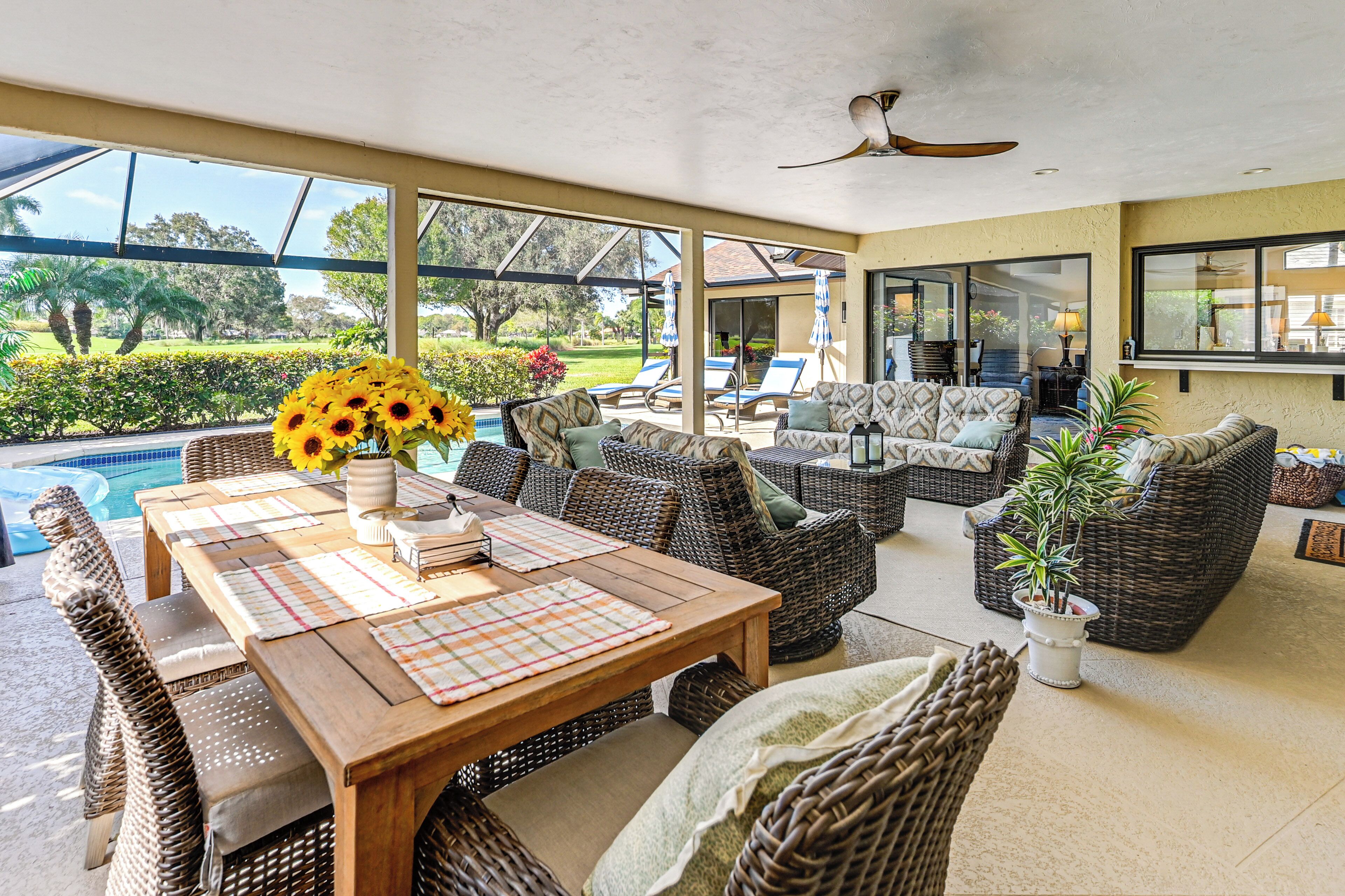 A covered outdoor area with wicker furniture, a wooden table, and a view of a swimming pool and garden.