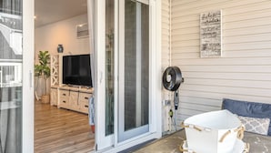 Un salon moderne avec une porte-fenêtre coulissante, un téléviseur à écran plat, un ventilateur et une baignoire blanche sur une terrasse.