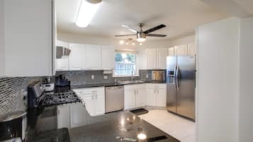 A modern kitchen with white cabinets, a black countertop, stainless steel appliances, and a ceiling fan.