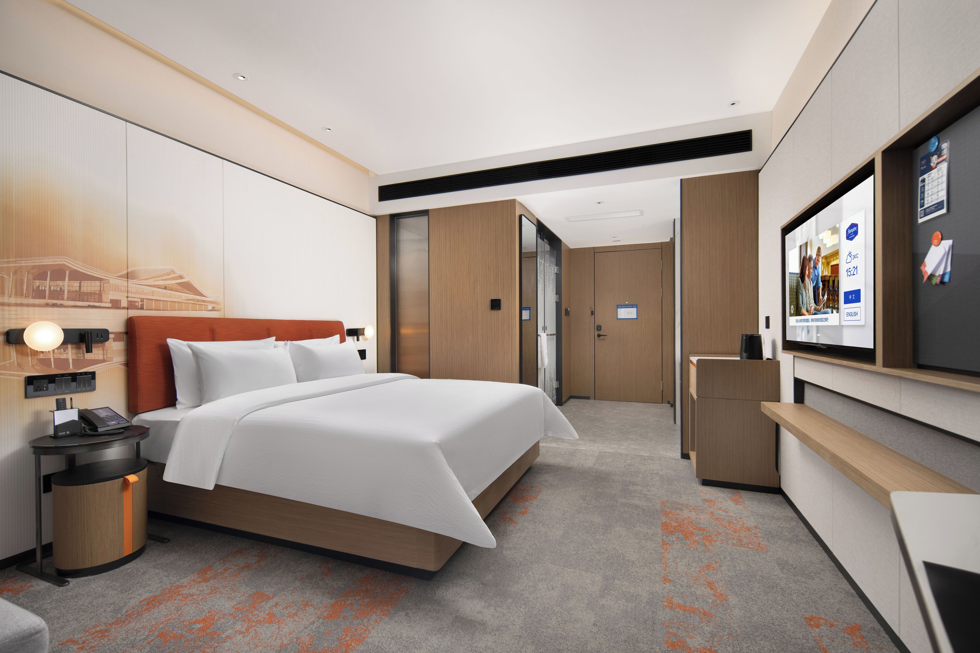 A modern hotel room with a large bed, a desk, a TV, and a bathroom visible through an open door.