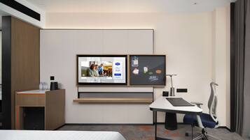 Habitación de hotel con una cama, un escritorio con silla, un televisor montado en la pared y un mueble auxiliar pequeño.