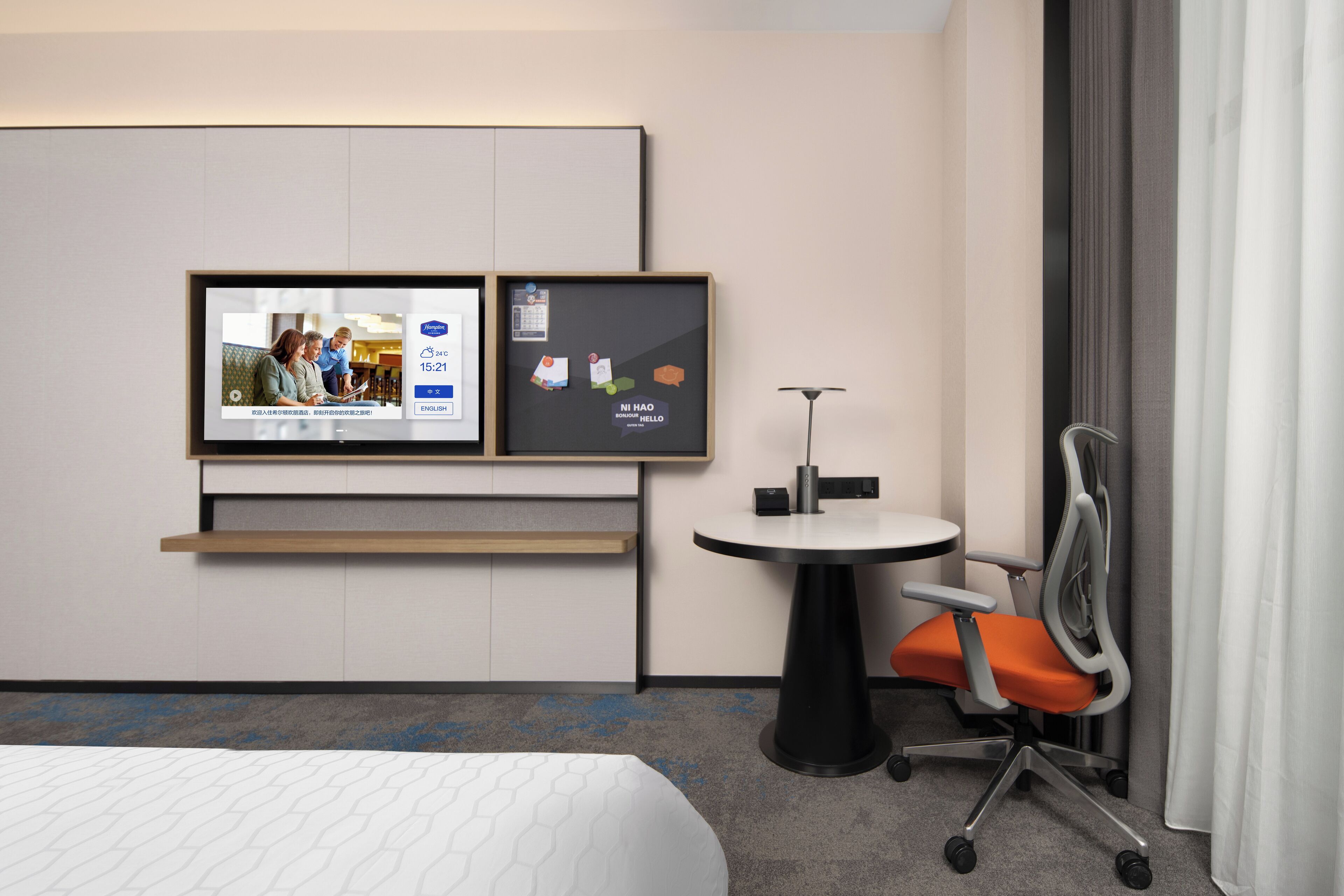 A hotel room with a bed, a TV mounted on the wall, a small round table with a chair, and a desk with a chair.