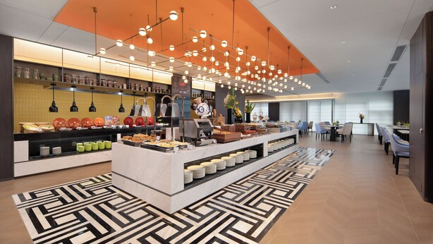 A modern hotel lobby with a buffet area, seating arrangements, and a patterned floor. - Hampton by Hilton Yichun  (Yichun)