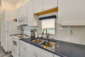 A modern kitchen with white cabinets, a stainless steel sink, a microwave, and a stove. - New Home on Lake Michigan's Traverse City West Bay (Traverse City)