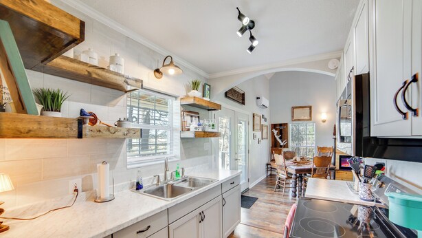 A kitchen with white cabinets, wooden shelves, a black stove, and a dining area with a table and chairs. - Anglers' Haven! Cedar Creek Reservoir Getaway (Tool)