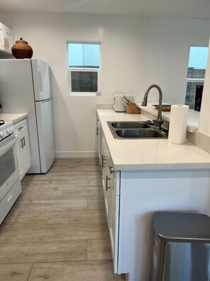 A modern kitchen with white cabinetry, a stainless steel sink, a built-in oven, and a window above the sink. - Brand-New Home. Great Location. Monthly Discounts (Los Angeles)