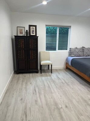 A bedroom with a bed, a window, a chair, and a dark wooden cabinet with books. - Brand-New Home. Great Location. Monthly Discounts (Los Angeles)