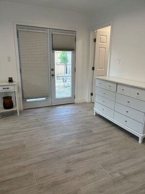 Ein Zimmer mit einer Schiebetür zum Garten, einem weißen Schminktisch und einem kleinen Tisch mit einer Vase.