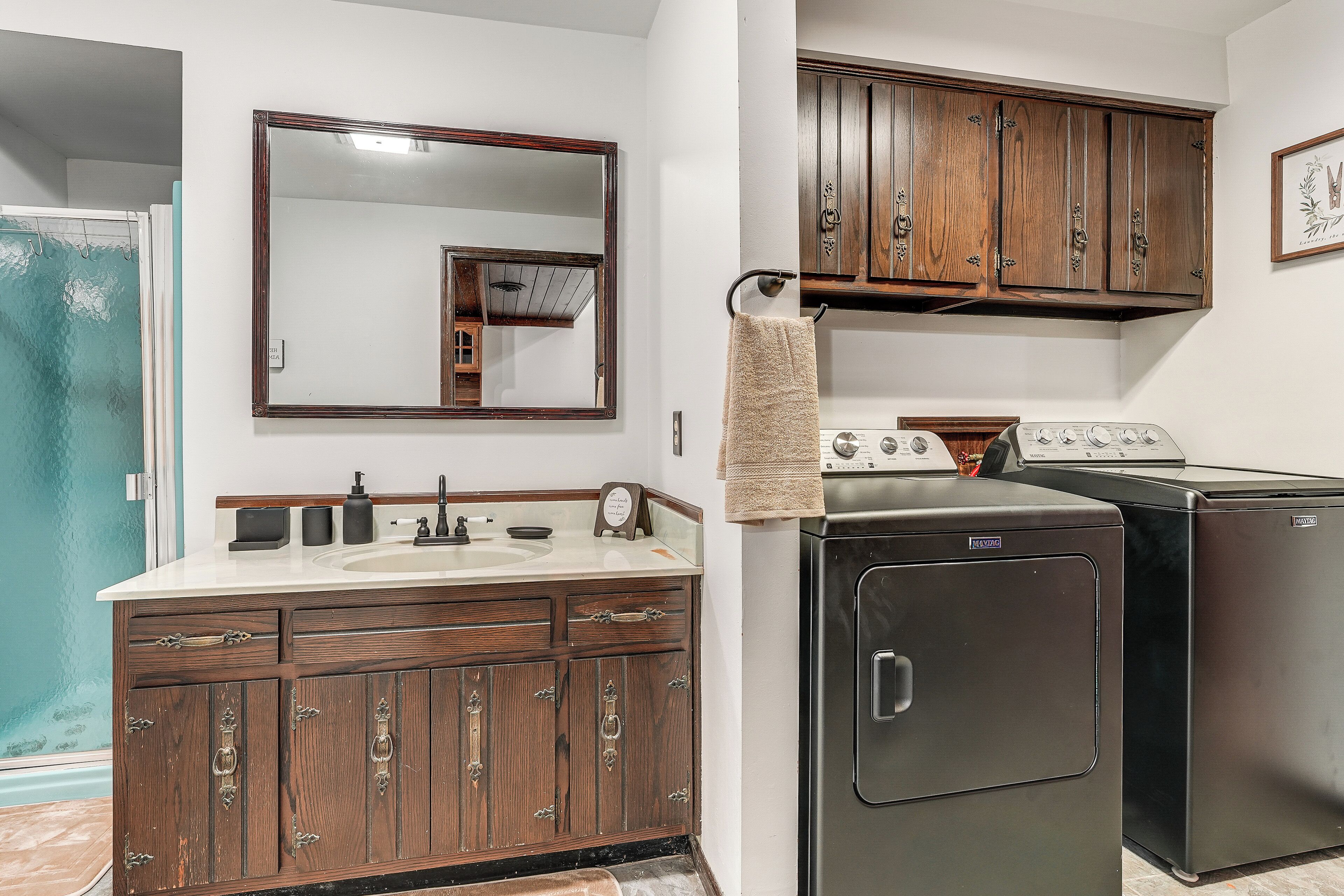 A bathroom with a wooden vanity, a mirror, a sink, and a washing machine.