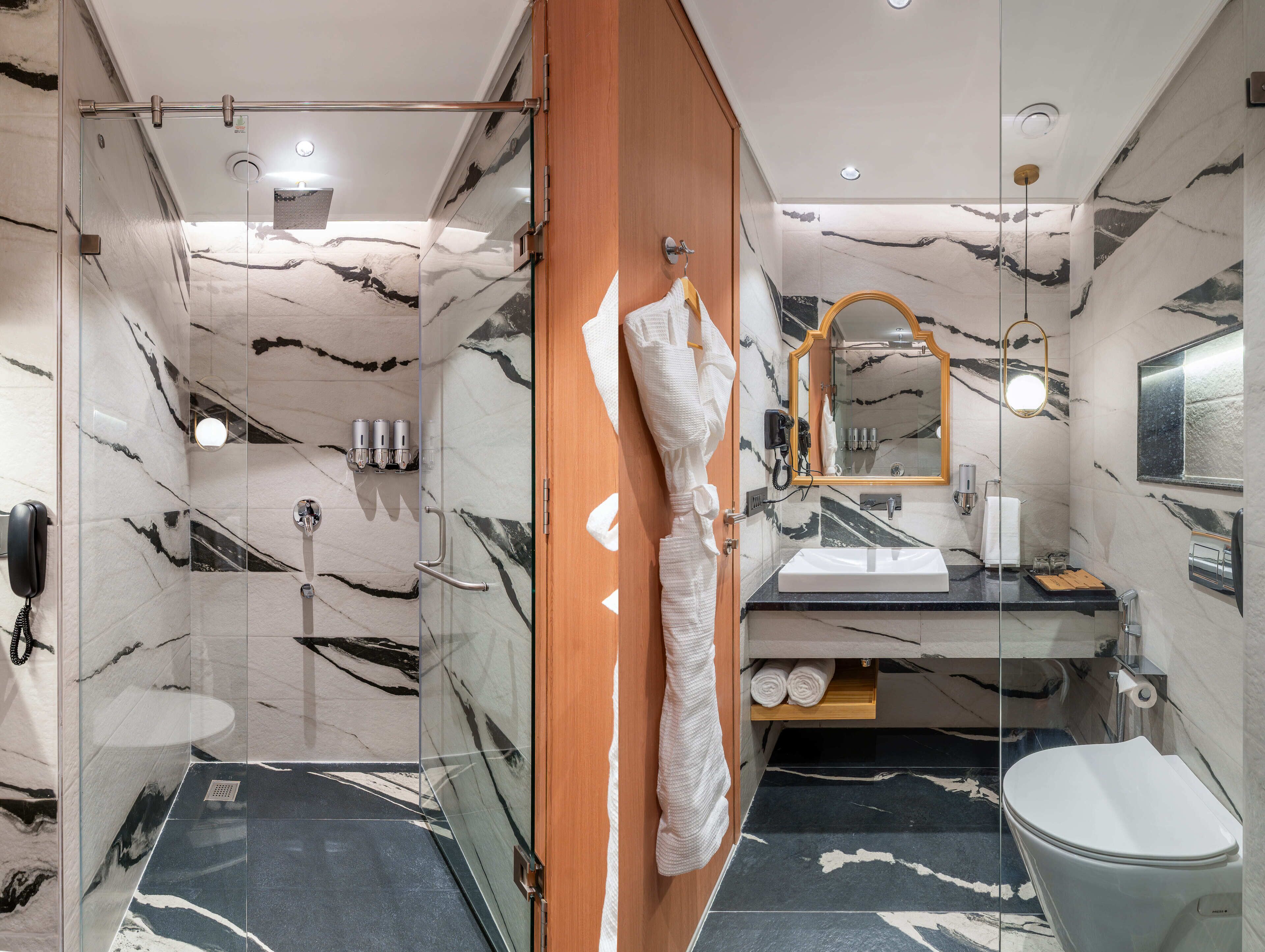 A modern bathroom with a glass shower enclosure, a wooden door, a marble-tiled floor, a sink with a mirror, and a toilet.