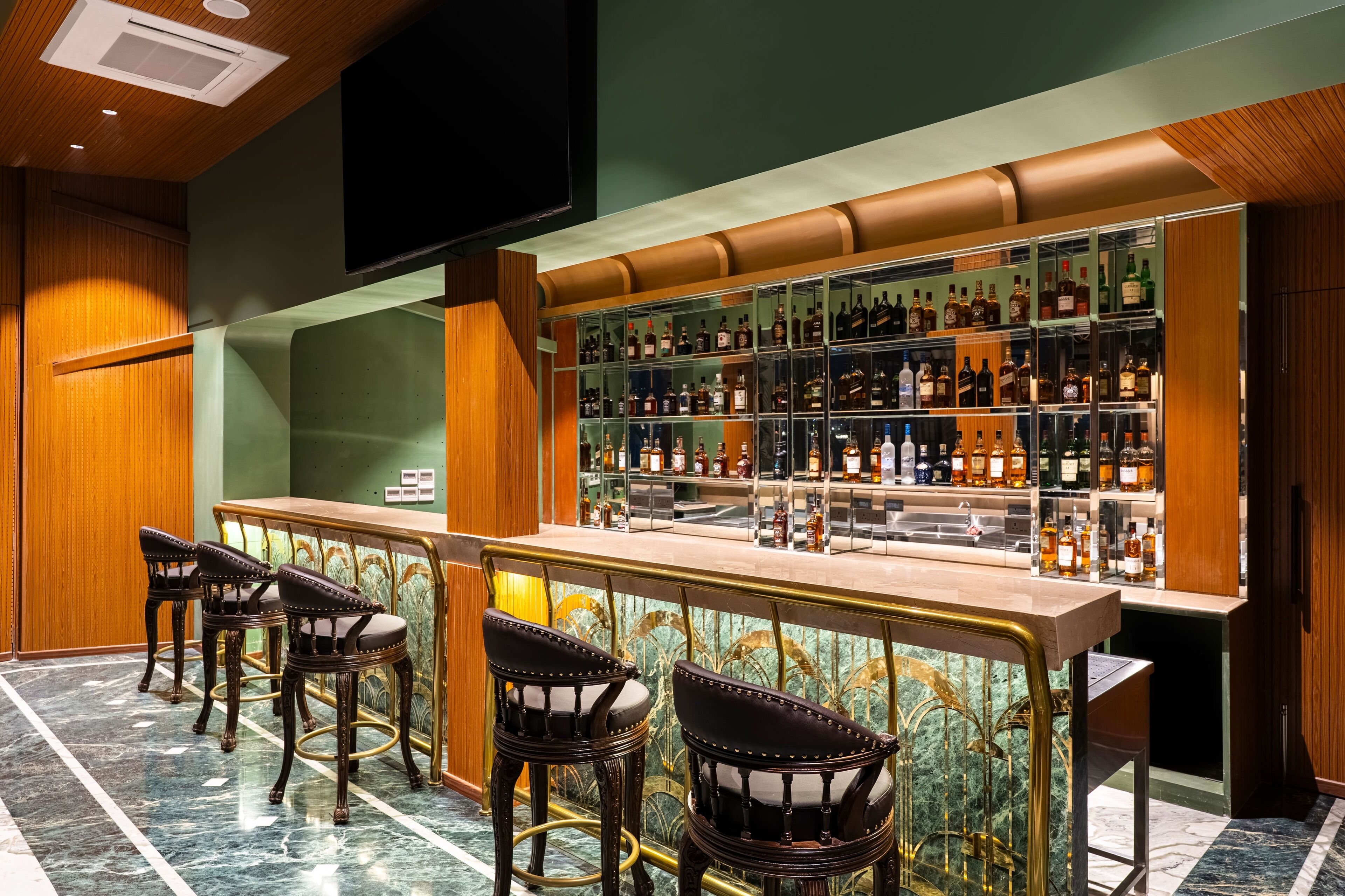 Zona de bar con suelo de mármol, mostrador de madera y varios taburetes.