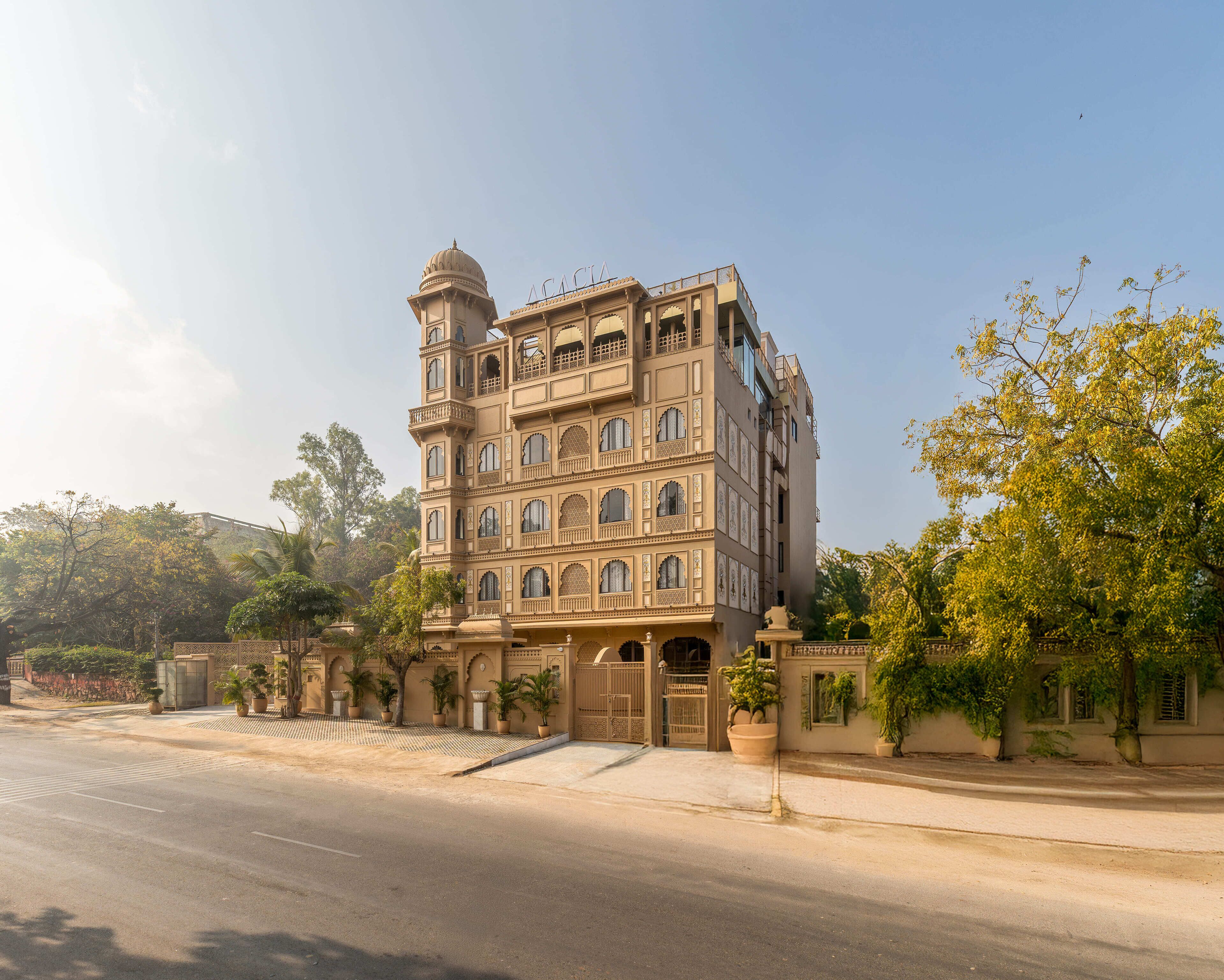 A multi-story building with a prominent dome and arched windows, surrounded by greenery and a paved street.