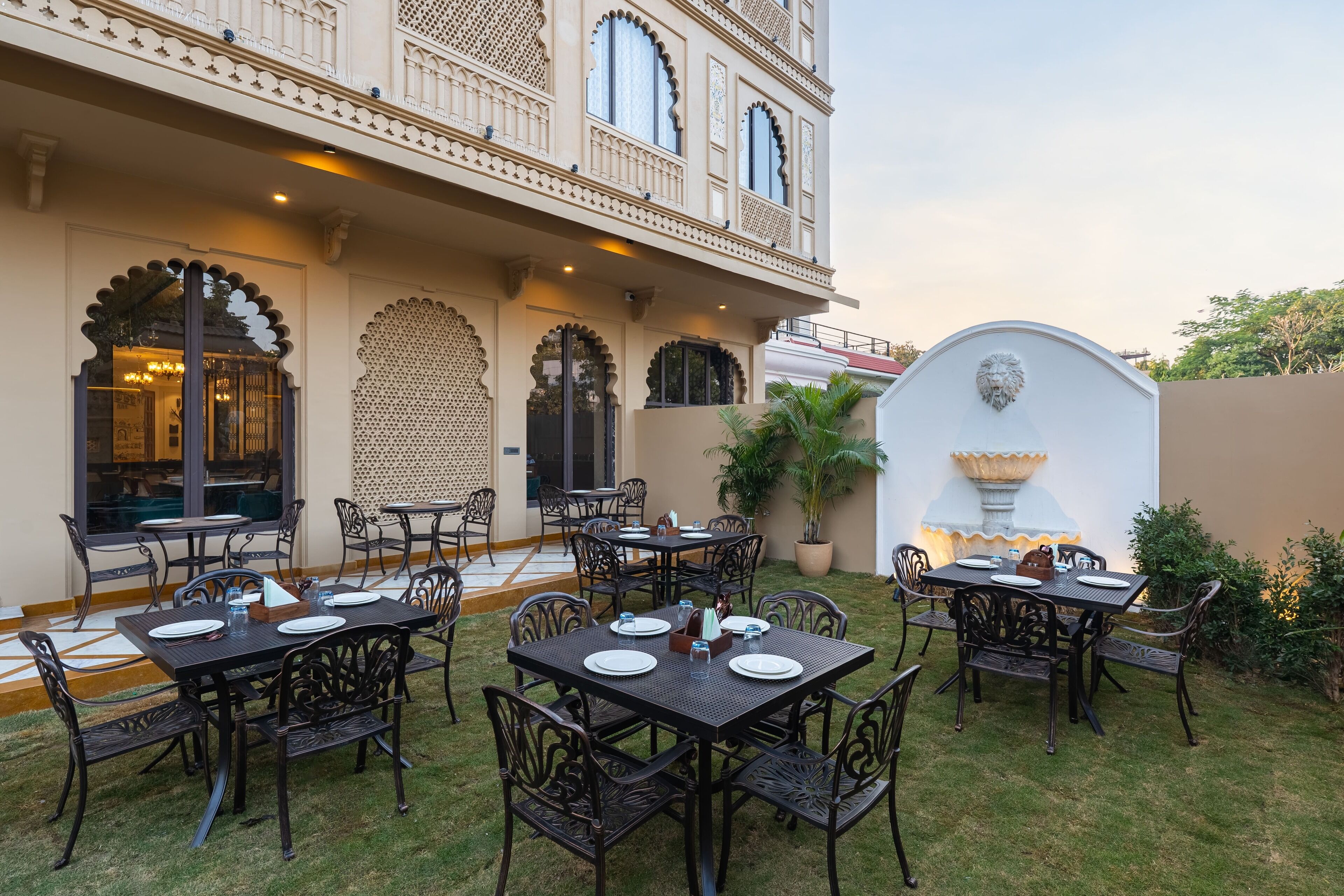 An outdoor dining area with multiple tables and chairs, a decorative wall, and a fountain.