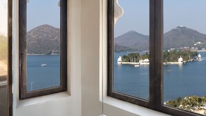 Vista desde una ventana con barandilla metálica, sobre un cuerpo de agua con barcos y una colina distante.