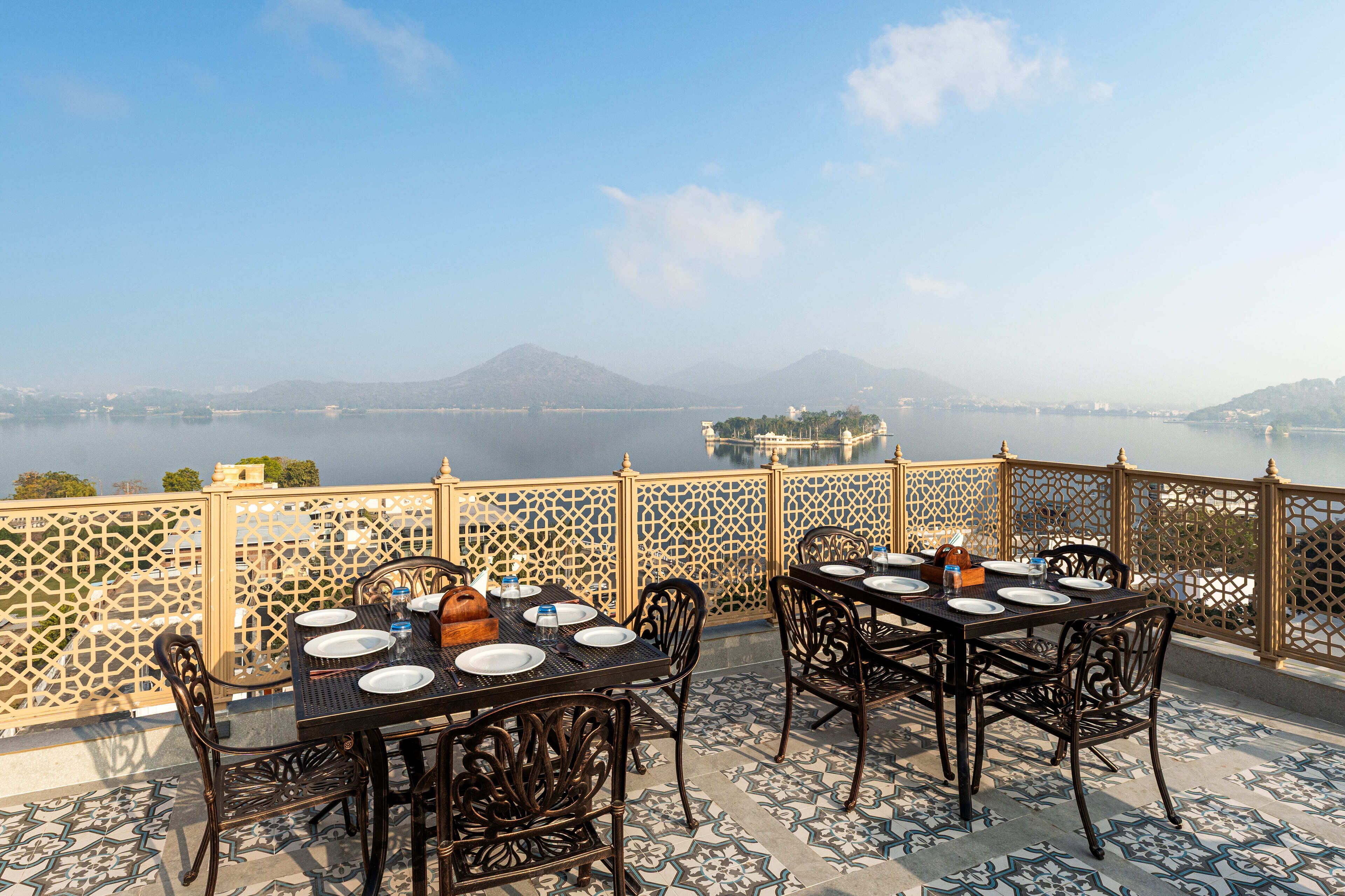A terrace with tables set for dining, overlooking a body of water and distant mountains.