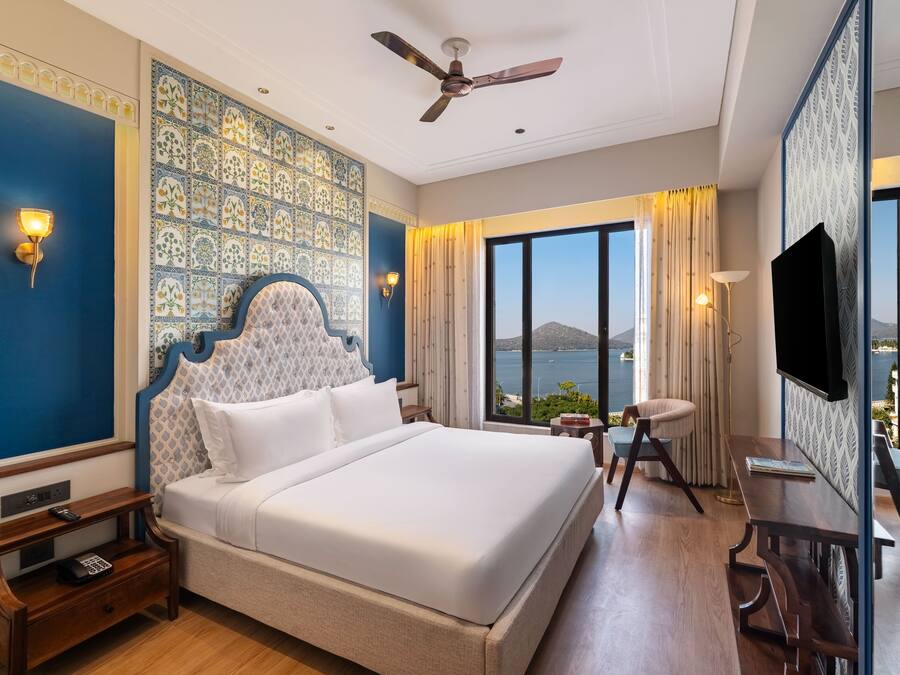 A hotel room with a large bed, a desk, a chair, a TV, and a view of the sea.