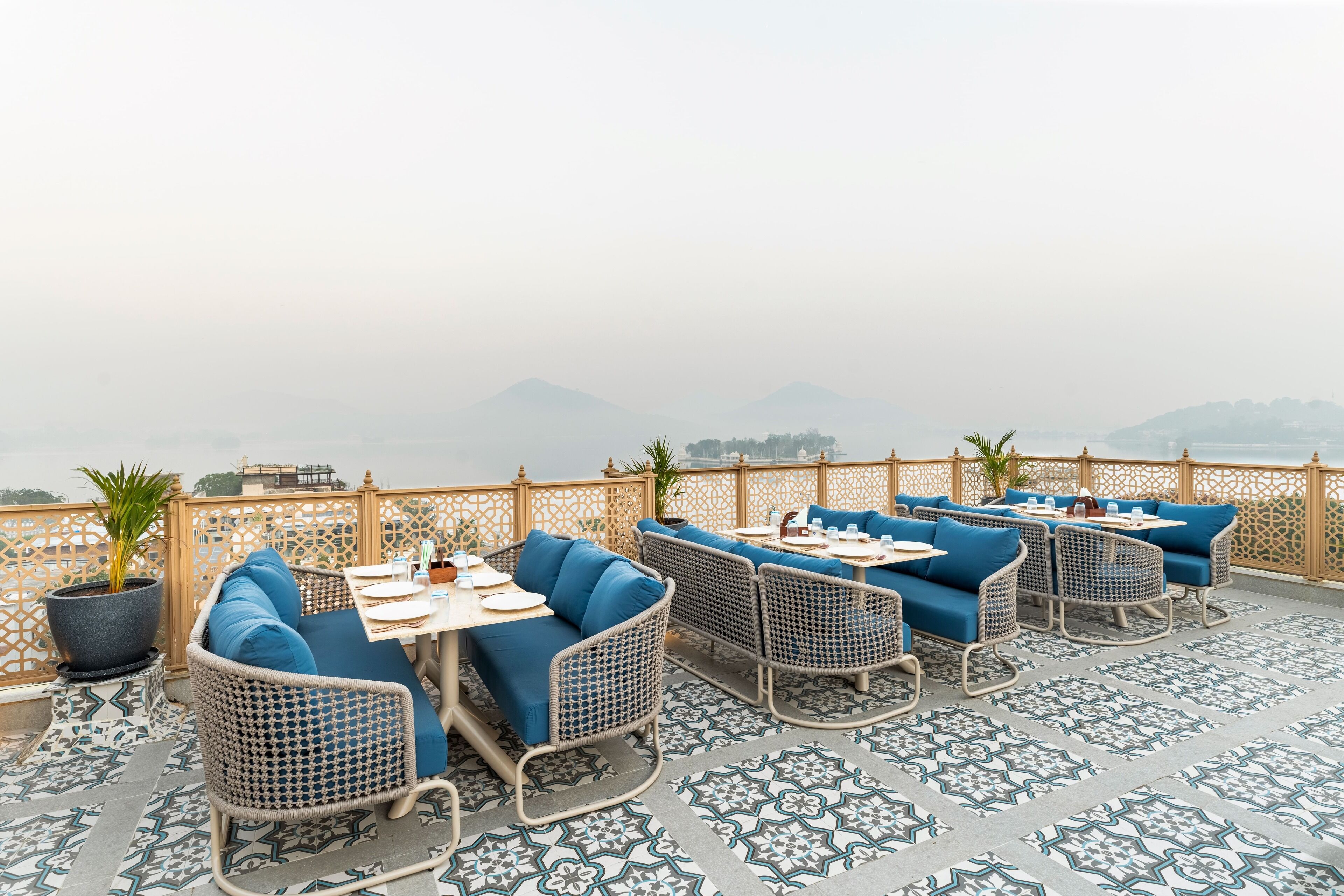 A terrace with wicker furniture and patterned flooring, overlooking a mountainous landscape.