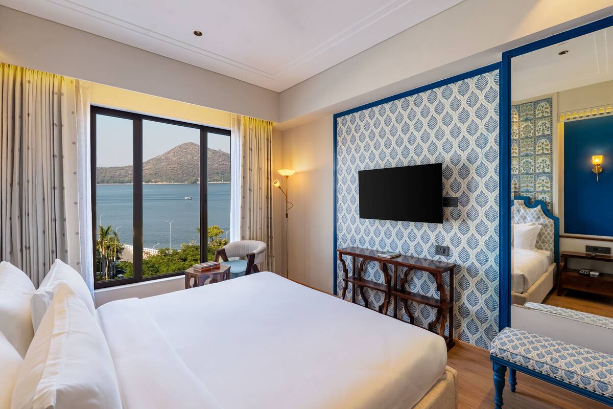 A hotel room with a large bed, a desk, a chair, a TV, and a view of the sea.