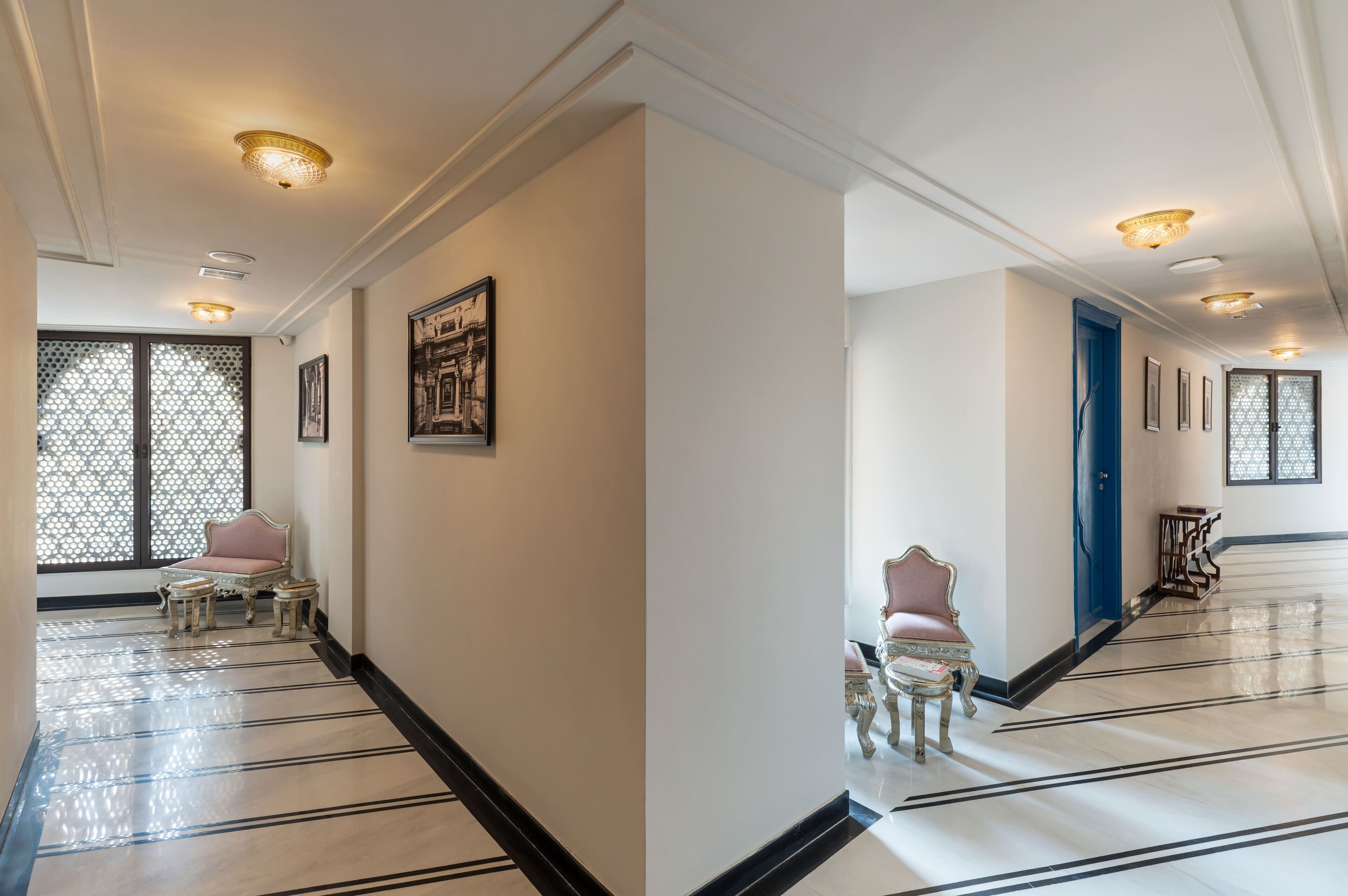 A hallway with a patterned floor, a blue door, and a seating area with a pink chair and a small table.