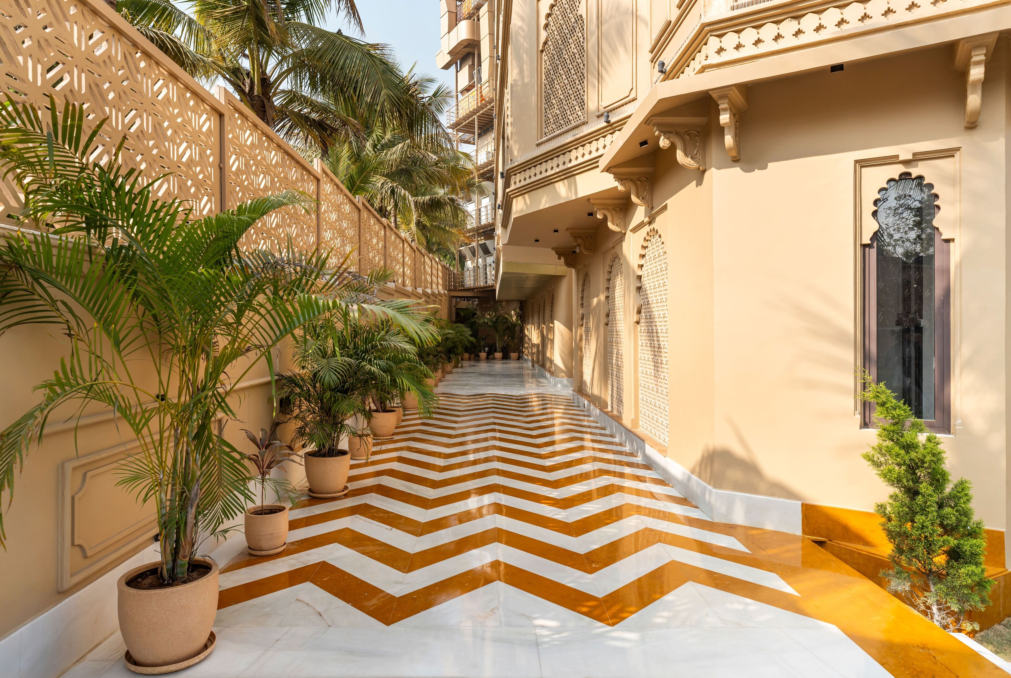 Un couloir dont le sol est orné d’un motif en chevrons, agrémenté de plantes en pot et présentant des éléments architecturaux traditionnels.