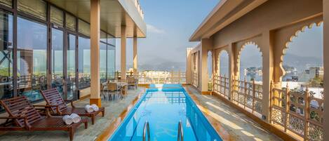 A rooftop pool with wooden loungers and a clear view of the cityscape.