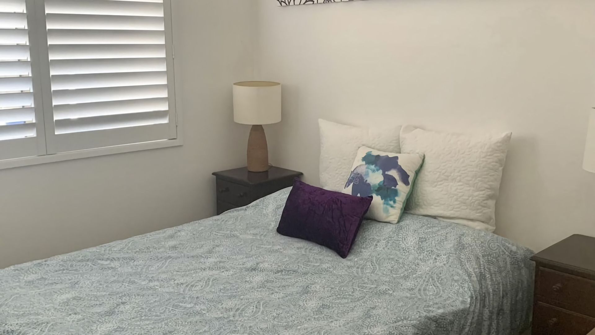 Une chambre à coucher avec un lit, une table de chevet, une lampe et une fenêtre avec des stores.