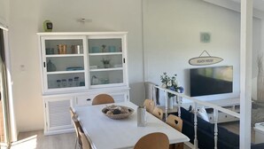 Zona pranzo con tavolo bianco, sedie e un mobile con ante in vetro.