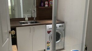 Une petite cuisine équipée d’un évier, d’un lave-linge et d’un miroir placé au-dessus de l’évier.