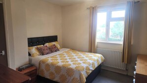 Una camera da letto con un letto, un comodino, una finestra con tende e un termosifone.