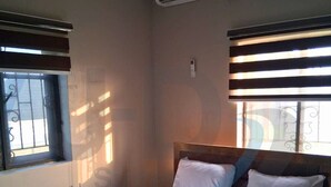 A bedroom with a bed, air conditioning unit, window with blinds, and a wall-mounted light switch. - J-D Suites (Ozuoba)