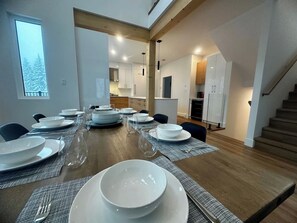 Zona pranzo con un tavolo lungo apparecchiato per un pasto, una cucina sullo sfondo e una scala che conduce a un livello superiore.
