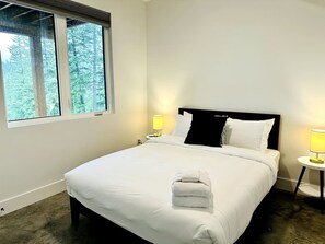 Camera d'albergo con un letto grande, due abat-jour, una finestra con vista sugli alberi e un letto rifatto con un asciugamano piegato.