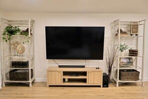 A living room with a flat-screen TV mounted on a wooden entertainment unit, flanked by two white shelving units with decorative items and plants. - 2 Masters, Newly Renovated New Furnishings 4BR 3BA (San Diego)