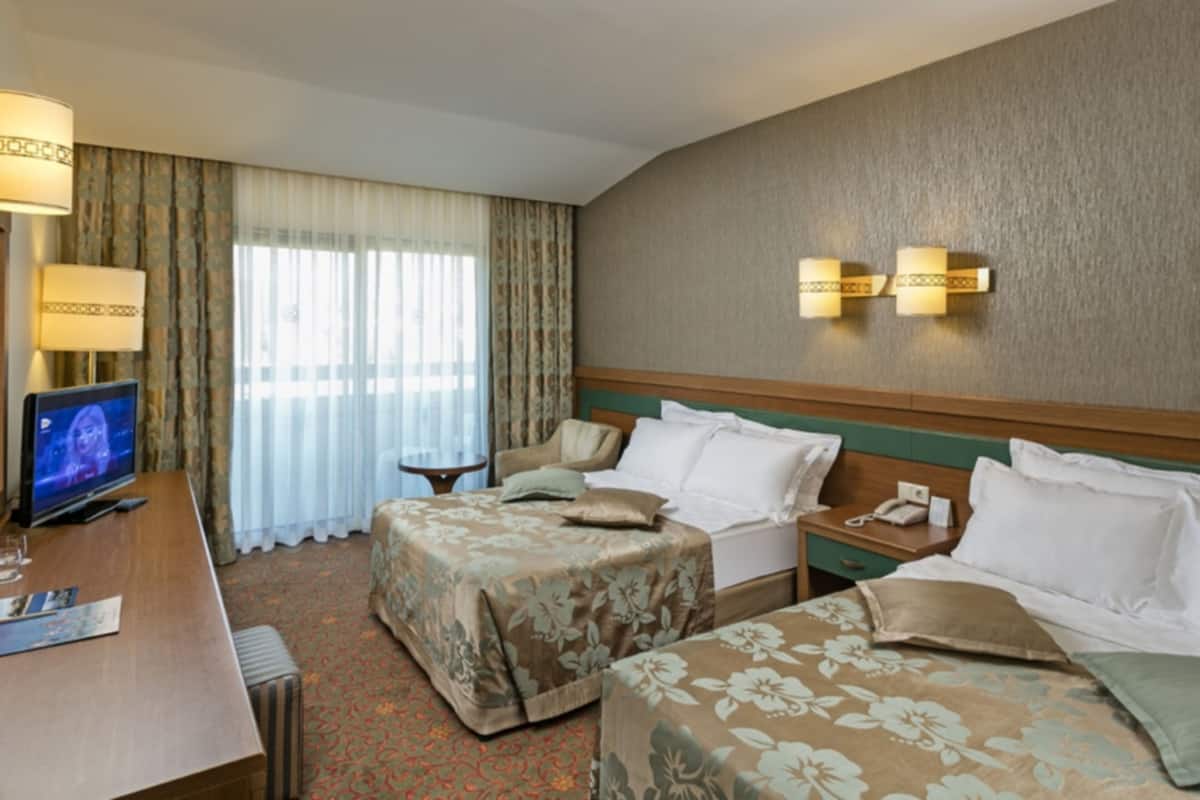 A hotel room with two beds, a desk, a TV, and a lamp.