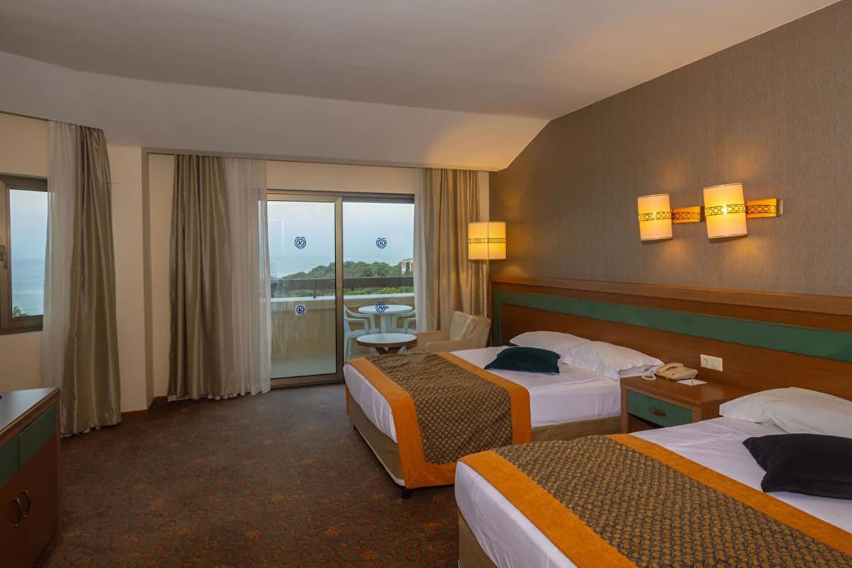 A hotel room with two beds, a small table, a chair, and a balcony with a view.