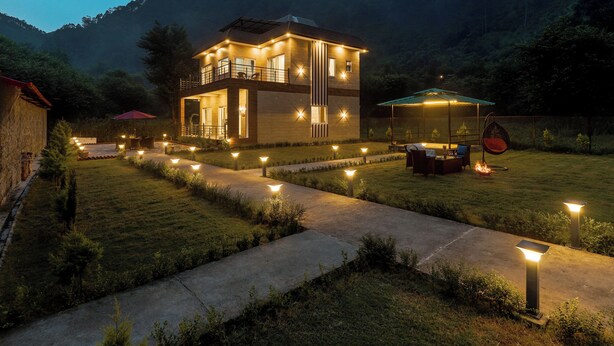 Ein zweistöckiges Haus mit Balkon, überdachter Terrasse und einem gut beleuchteten Garten im Abendlicht.