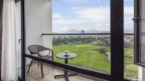 A balcony with a table and chair, offering a view of a green landscape and distant buildings. - RAY TOUR (Zhaoqing)