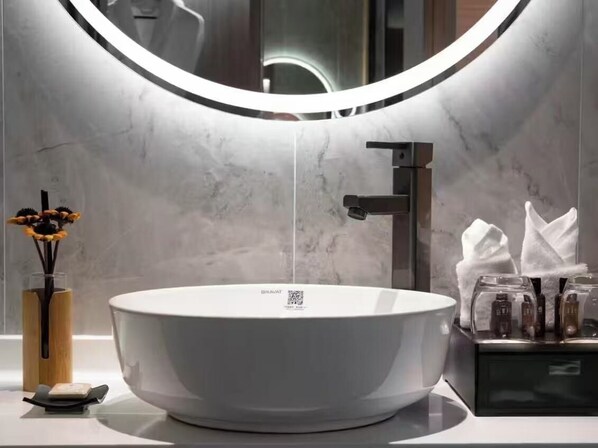 Un baño moderno con un lavabo grande tipo cuenco, un espejo con luz circular y un dispensador de toallas.